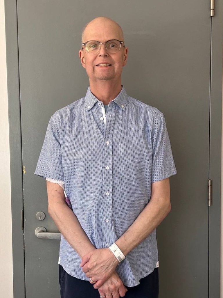 Mike Martineau standing in a hospital corridor wearing a patient wristband